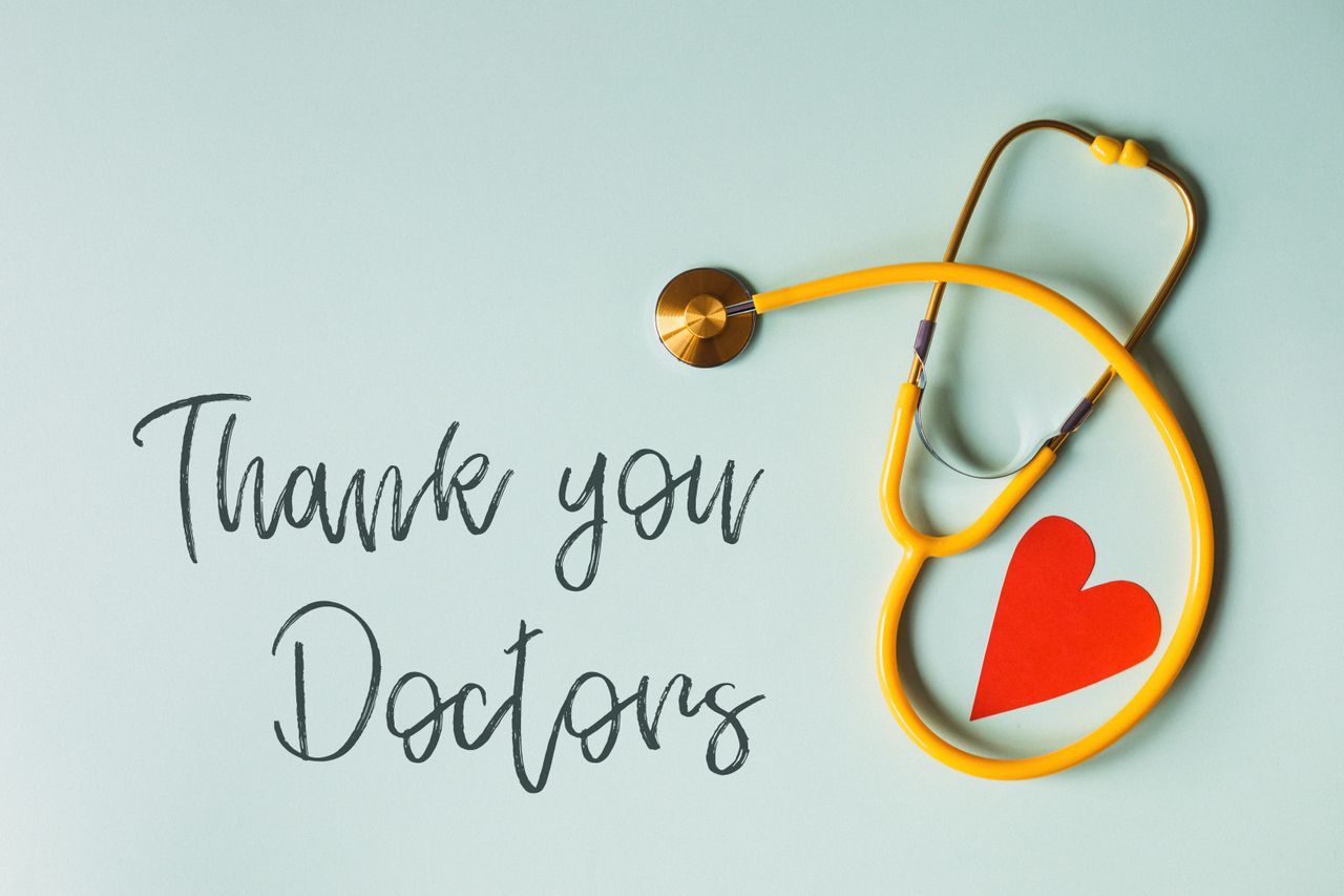 From above arrangement of yellow stethoscope with red heart shape placed on blue background with THANK YOU DOCTORS inscription